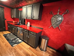 A kitchen with dark cabinets, a red countertop, and a decorative shield with swords.