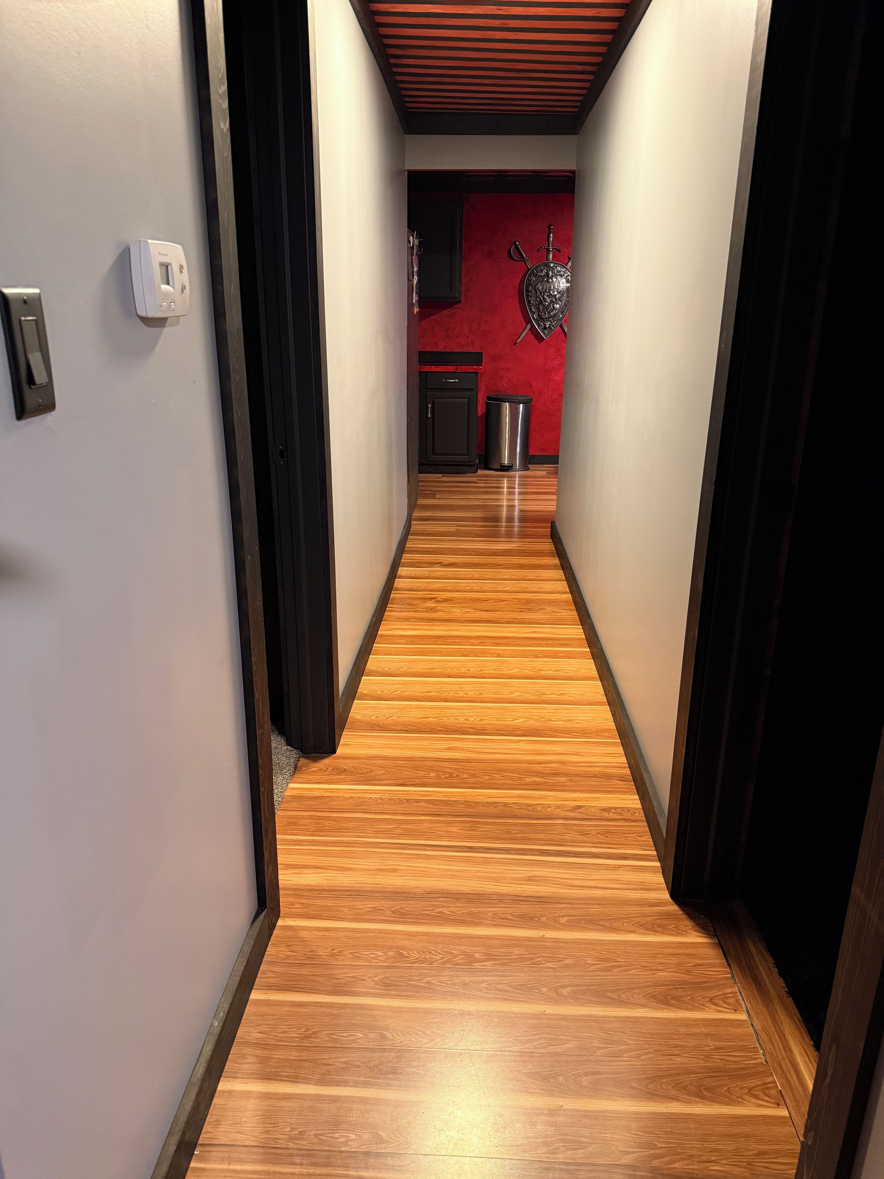 Un pasillo con suelo de madera, una pared de acento roja y un armario negro.