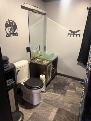 A bathroom with a glass sink, a toilet, and a mirror.