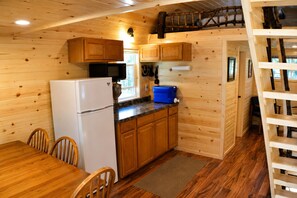 Une cuisine compacte avec des meubles en bois, un réfrigérateur, un four à micro-ondes et une glacière bleue posée sur le plan de travail.