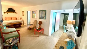A living room with a sofa, chairs, a coffee table, a TV, and a door leading to another room. - Waterfront cottage in Jensen Beach perfect for fishing, kayaking, and relaxing! (Jensen Beach)