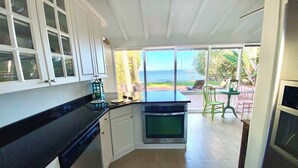 A kitchen with white cabinets, a black countertop, and a view of the sea through large windows. - Waterfront cottage in Jensen Beach perfect for fishing, kayaking, and relaxing! (Jensen Beach)