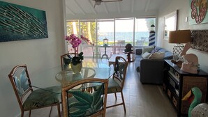 A spacious living area with a glass dining table, wicker chairs, a ceiling fan, and a view of the sea. - Waterfront cottage in Jensen Beach perfect for fishing, kayaking, and relaxing! (Jensen Beach)
