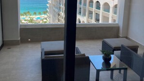 Uma varanda com vista para o oceano e um edifício de resort. Há duas cadeiras e uma mesa com uma planta.
