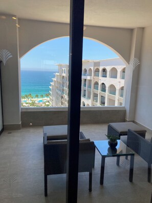 Ein Balkon mit Blick auf den Ozean und ein Hotelgebäude. Zwei Stühle und ein Tisch mit einer Pflanze darauf.