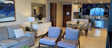 A modern living room with a sofa, armchairs, a coffee table, and a dining area with a table set for four.