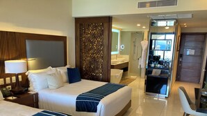 Quarto de hotel com duas camas, uma escrivaninha, uma cadeira, banheiro e uma cozinha compacta.