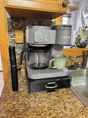 Una cafetera Keurig con un dispensador manual de cápsulas de café sobre una encimera de granito.