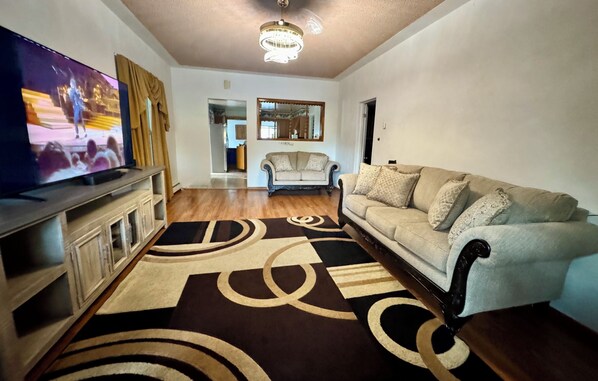 Una sala de estar con televisor, sofá, alfombra estampada y candelabro.