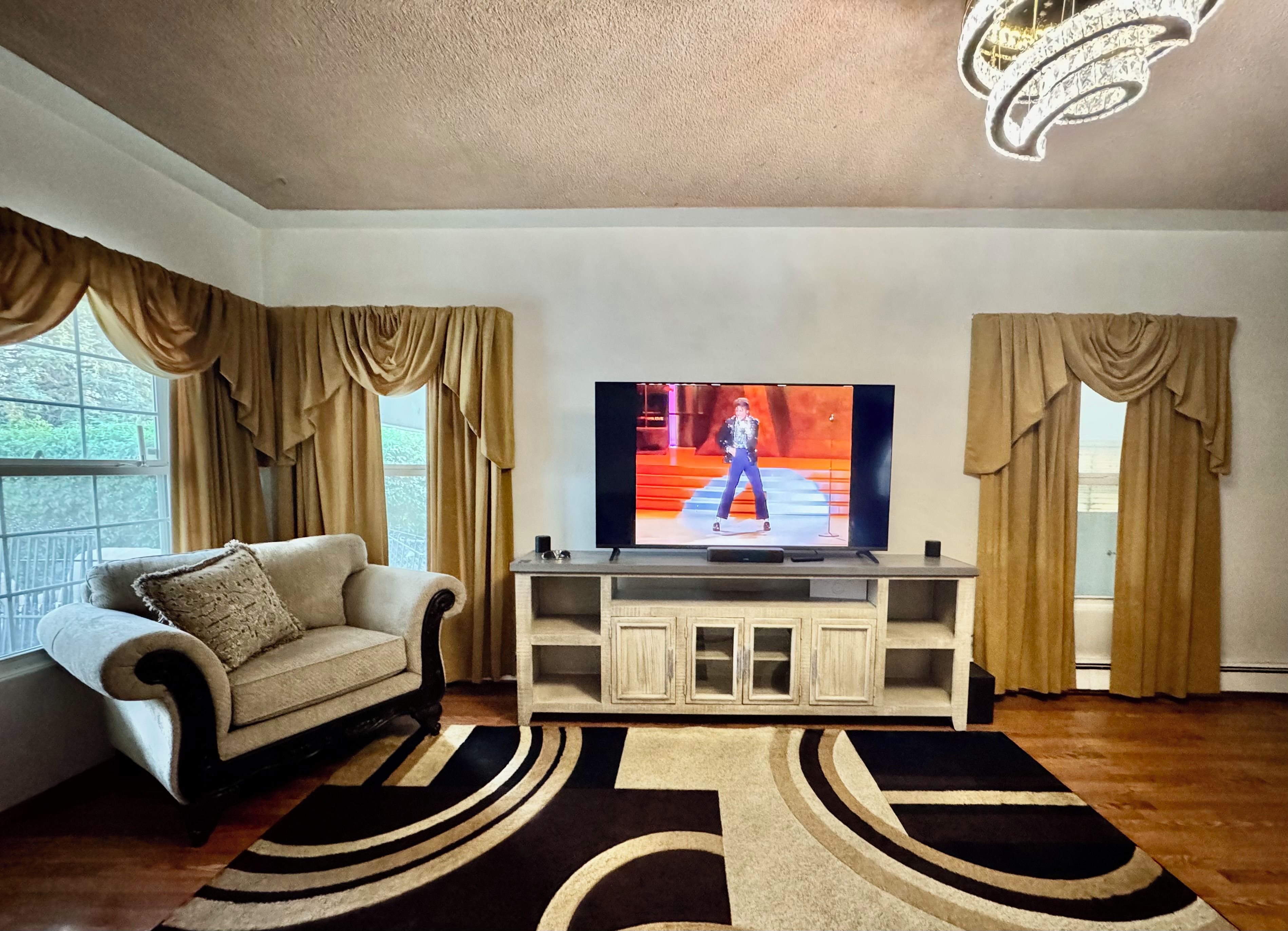 Una sala de estar con televisor, un sofá, un mueble aparador y una alfombra estampada.