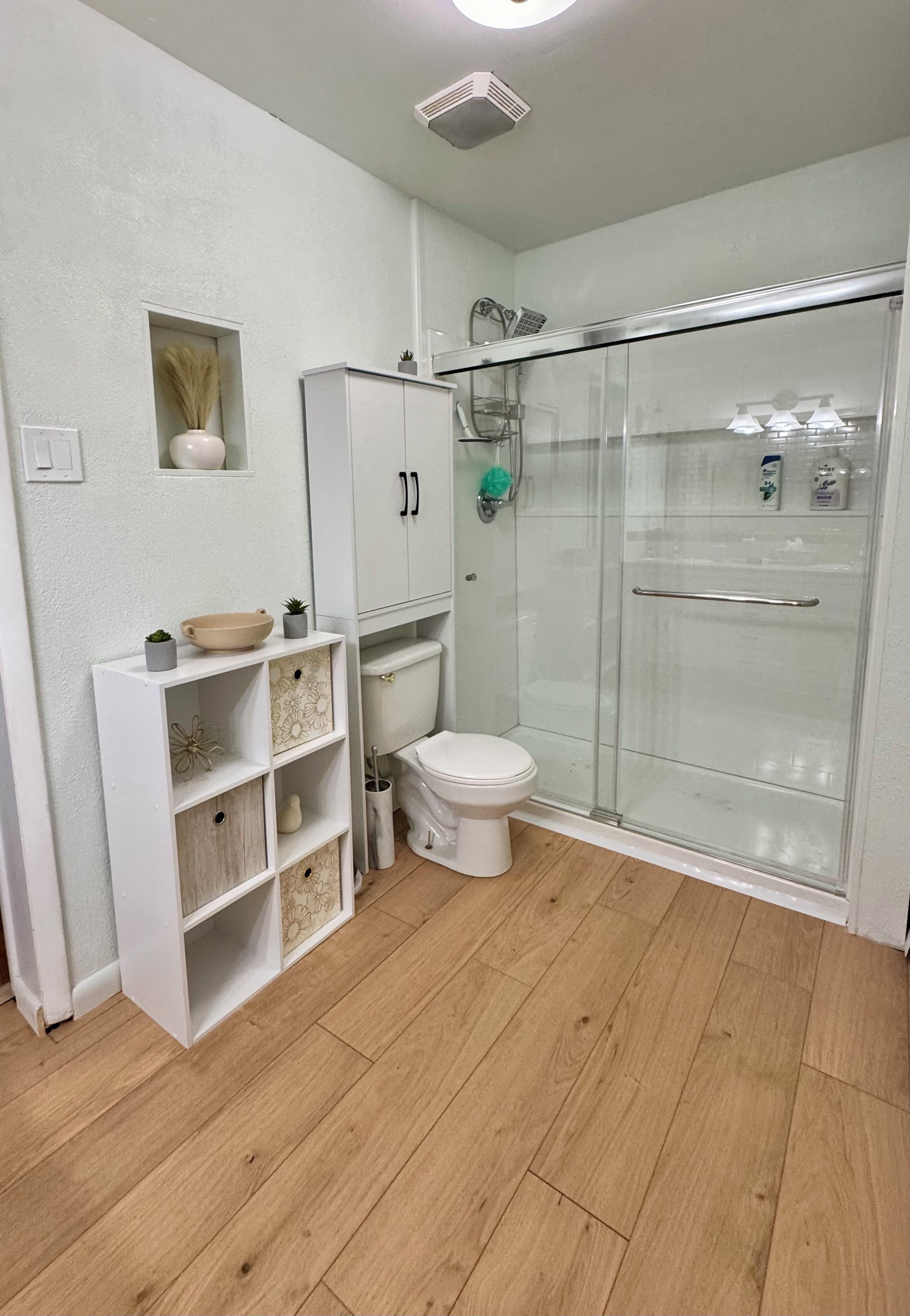 A bathroom with a toilet, a shower enclosure, and a vanity with shelves.