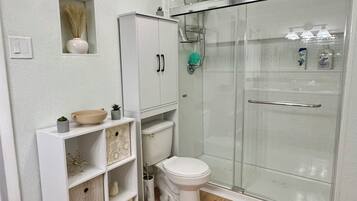 A bathroom with a toilet, a shower enclosure, and a vanity with shelves.