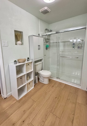 Un baño con inodoro, cabina de ducha y tocador con estantes.