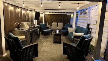 An outdoor patio area with a grill, seating, and a TV screen.