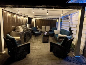 An outdoor patio area with a grill, seating, and a TV screen.