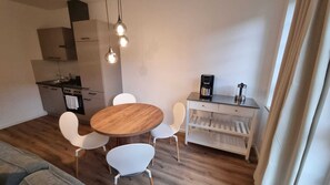 A compact kitchen with a dining area, including a wooden table and white chairs, a coffee machine, and a cabinet. - Landungsbrücken Suite (Hamburg)