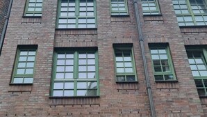 Un edificio in mattoni di più piani, con cornici verdi alle finestre e una scala antincendio visibile.