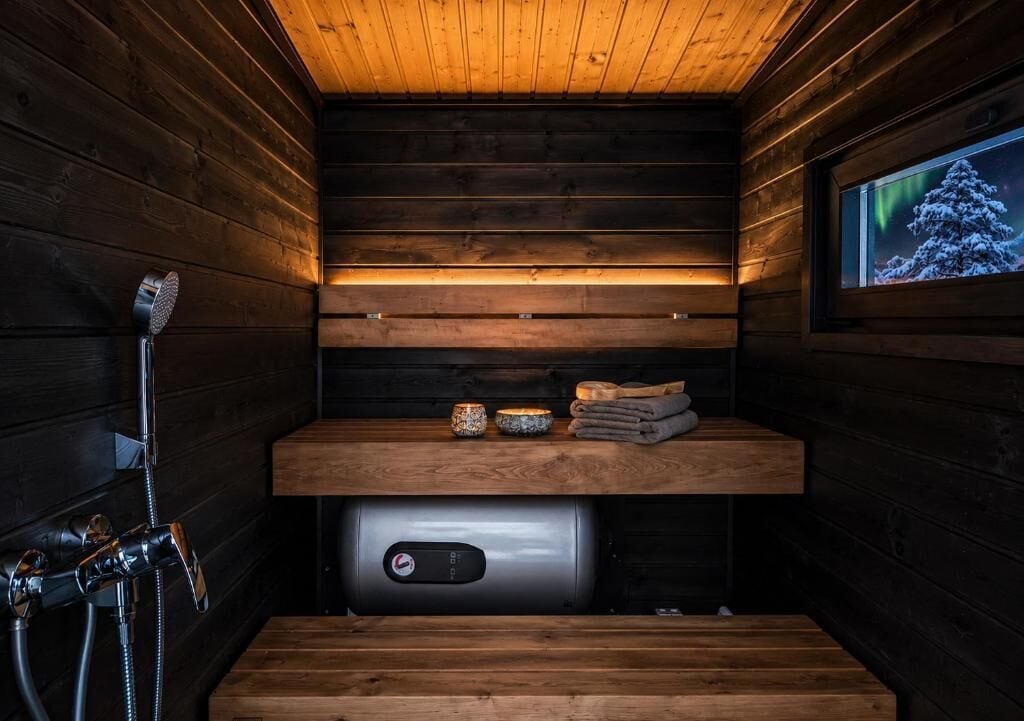 Un cuarto de sauna con paredes de madera, un banco, un calentador y una ventana con vista a la aurora boreal.