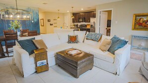Ein Wohnzimmer mit einem weißen Sofa, einem braunen Ottomanen und einem Essbereich mit Holzsesseln und einem Tisch.