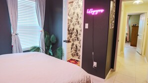 Ein Schlafzimmer mit Bett, Vorhängen, einer Tür mit floralem Muster und einem Neonzeichen.