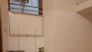 Une pièce avec un téléviseur posé sur un meuble en bois, un lit recouvert d’une couvre-lit à motifs orange et une fenêtre avec des barreaux en métal.