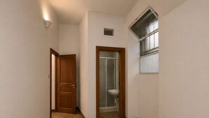 Un couloir avec une porte en bois, une salle de bain avec un lavabo et une fenêtre à vitre dépolie.