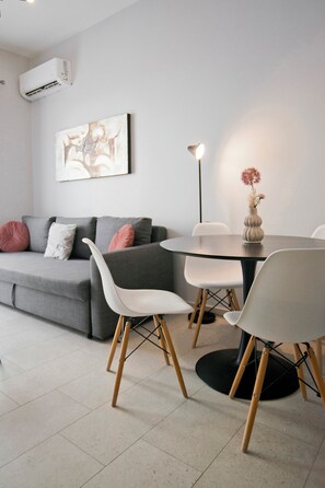 Ein modernes Wohnzimmer mit einem grauen Sofa, weißen Sesseln, einem runden Tisch und einer Stehlampe.