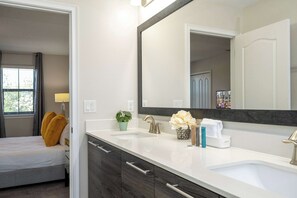 Une salle de bain moderne avec un grand miroir, un lavabo blanc et un lit donnant sur une fenêtre.