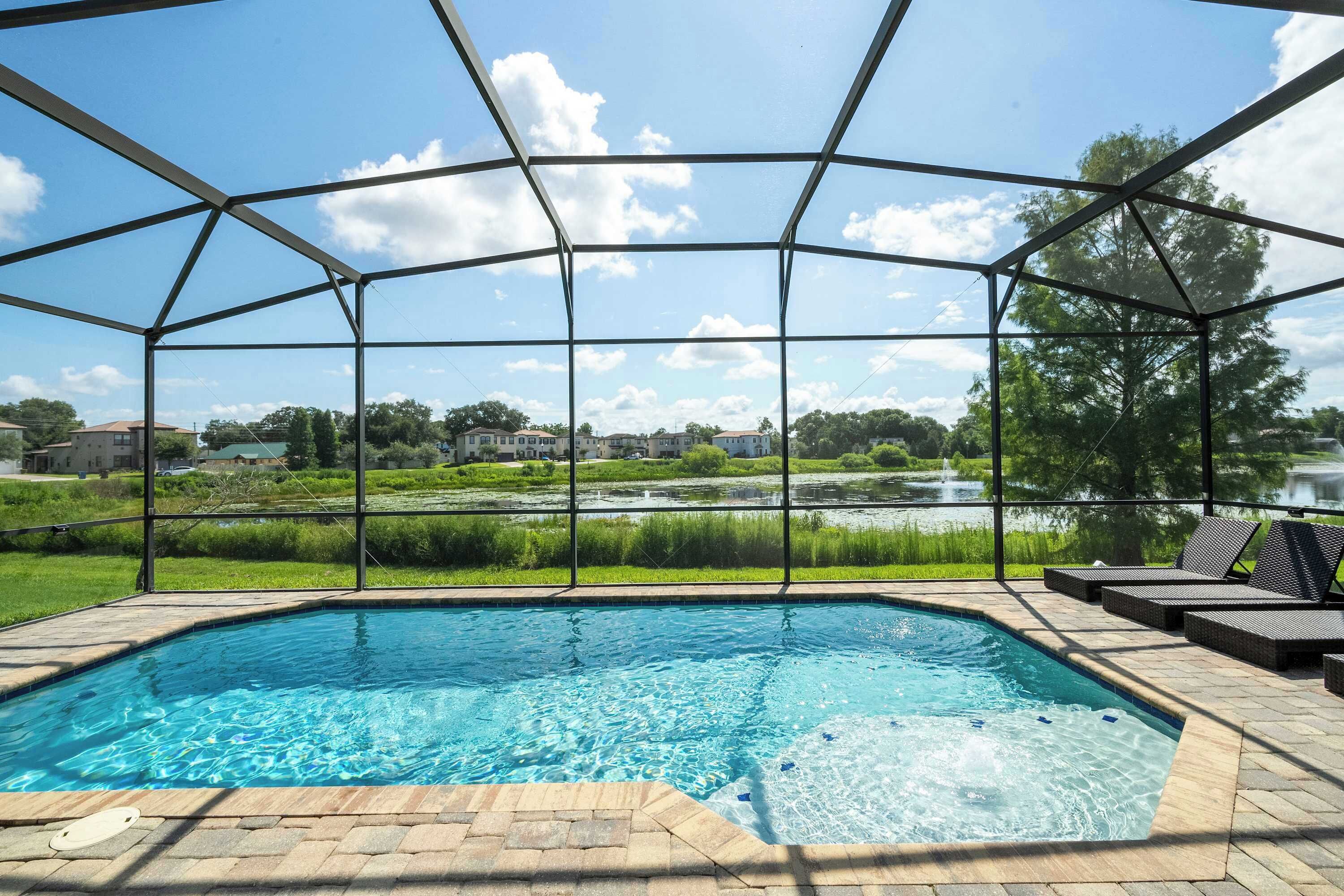 A swimming pool with a view of a lake and houses, surrounded by a covered area with lounge chairs.