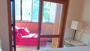 Une chambre avec un lit, une table de chevet, une lampe, un tapis et une porte-fenêtre coulissante donnant sur un espace extérieur avec un canapé rouge.