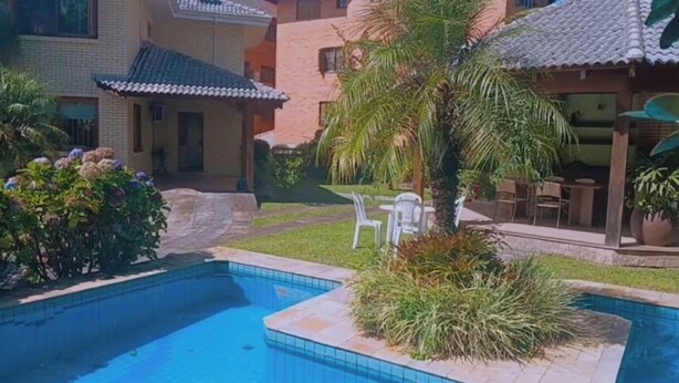 Une piscine dotée d’une terrasse carrelée, entourée de verdure et bordée d’un bâtiment dont le toit est également recouvert de tuiles.