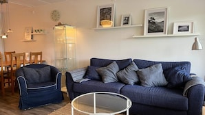 A living room with a blue sofa, a glass coffee table, and a dining area with wooden chairs and a table. - 5 Star Holiday Home in Uddevalla (Uddevalla)