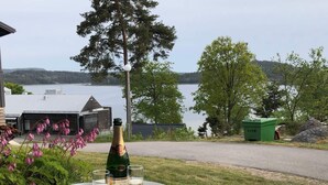 A table with a bottle of champagne, two glasses, and a bowl of snacks, set outdoors with a view of a lake and trees. - 5 Star Holiday Home in Uddevalla (Uddevalla)