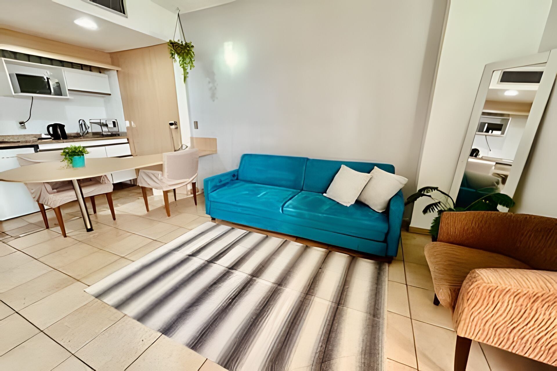 Una sala de estar moderna con un sofá azul, un tapete a rayas, una mesita con una planta y una cocina al fondo.