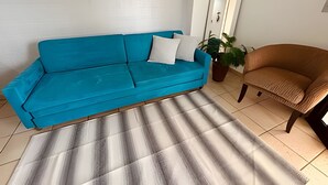 A room with a blue sofa, a brown armchair, and a striped rug. - SHB Horizonte Azul Refúgio Inesquecível (Santos)