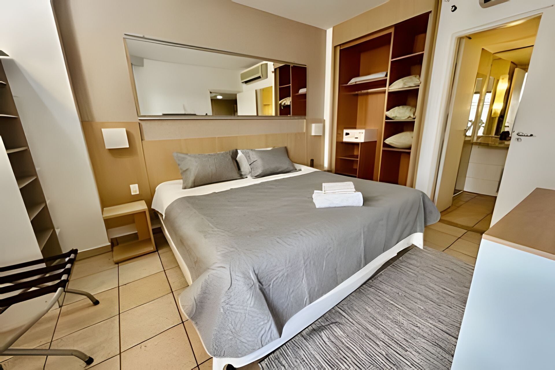 Un dormitorio ordenado con una cama grande, una mesita de noche, una silla, un armario y un espejo.