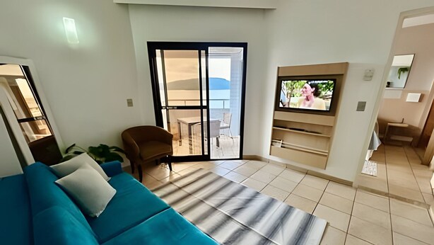 A living room with a blue sofa, a striped rug, and a TV mounted on the wall. - SHB Horizonte Azul Refúgio Inesquecível (Santos)
