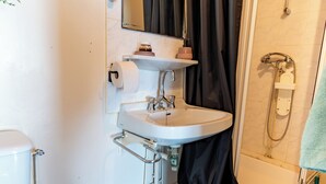 A bathroom with a white sink, a toilet, a shower, and a dark curtain. - Cozy, centrally located, quiet, and fully equipped studio—ideal for medical treatment, tourism, or business trips (Bourbonne-les-Bains)