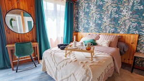 A bedroom with a bed, a bedside table, a chair, a mirror, and a window with curtains. - Cozy, centrally located, quiet, and fully equipped studio—ideal for medical treatment, tourism, or business trips (Bourbonne-les-Bains)