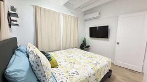 A bedroom with a bed, curtains, a TV, a plant, and a wardrobe. - Rycroft Residence 1BR Apt with AC & Full Kitchen (Honolulu)