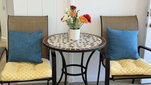 Two chairs with blue cushions and yellow patterned seats, a round table with a mosaic top, and a vase with red and orange flowers. - Rycroft Residence 1BR Apt with AC & Full Kitchen (Honolulu)