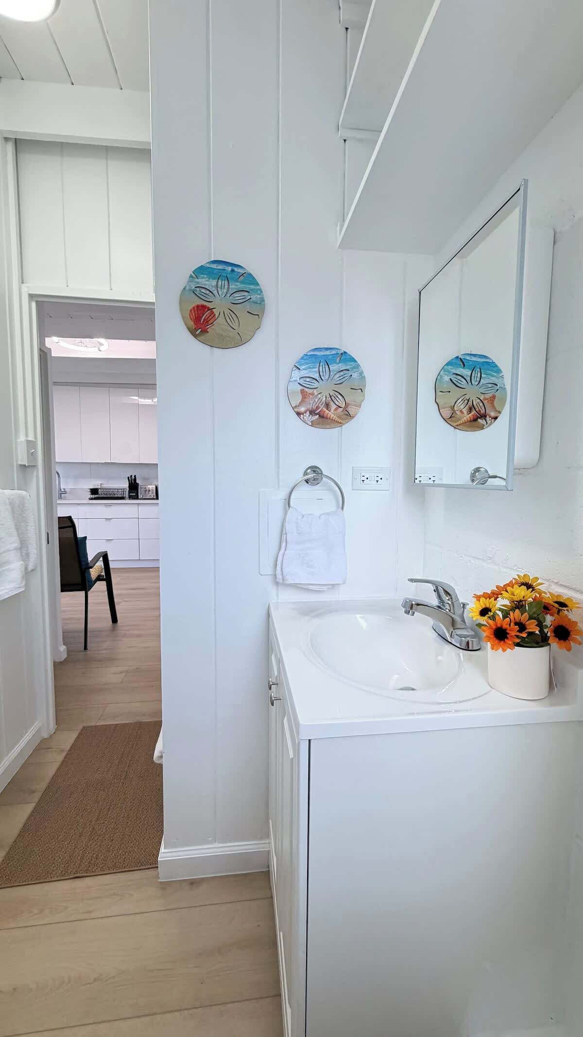 Une salle de bain moderne avec un lavabo blanc, un miroir et des œuvres d’art décoratives au mur.