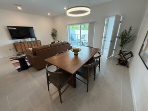 A modern living room with a sofa, a dining table with chairs, a flat-screen TV mounted on the wall, and a sliding glass door leading to an outdoor area. - 5 BD/ 4.5 BA/ New! Posner Reserve (125 PS) (Davenport)