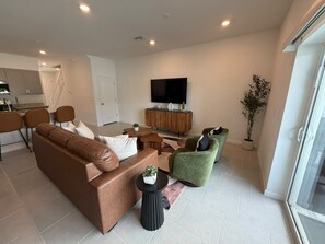 Ein modernes Wohnzimmer mit einem braunen Sofa, einem grünen Sessel und einem Flachbildfernseher auf einem Holzständer.