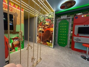 Ein Zimmer mit einer Wand im Nintendo-Design, einer grünen Tür und einer roten Arcade-Maschine.