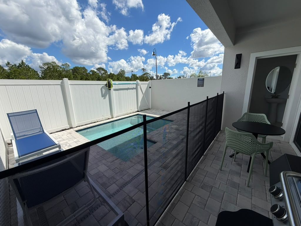 Un área de piscina en la azotea con barandilla de vidrio, una silla de descanso y una mesa con sillas.