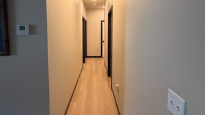 Un couloir doté d’un plancher en bois, de murs blancs et d’un luminaire au plafond.