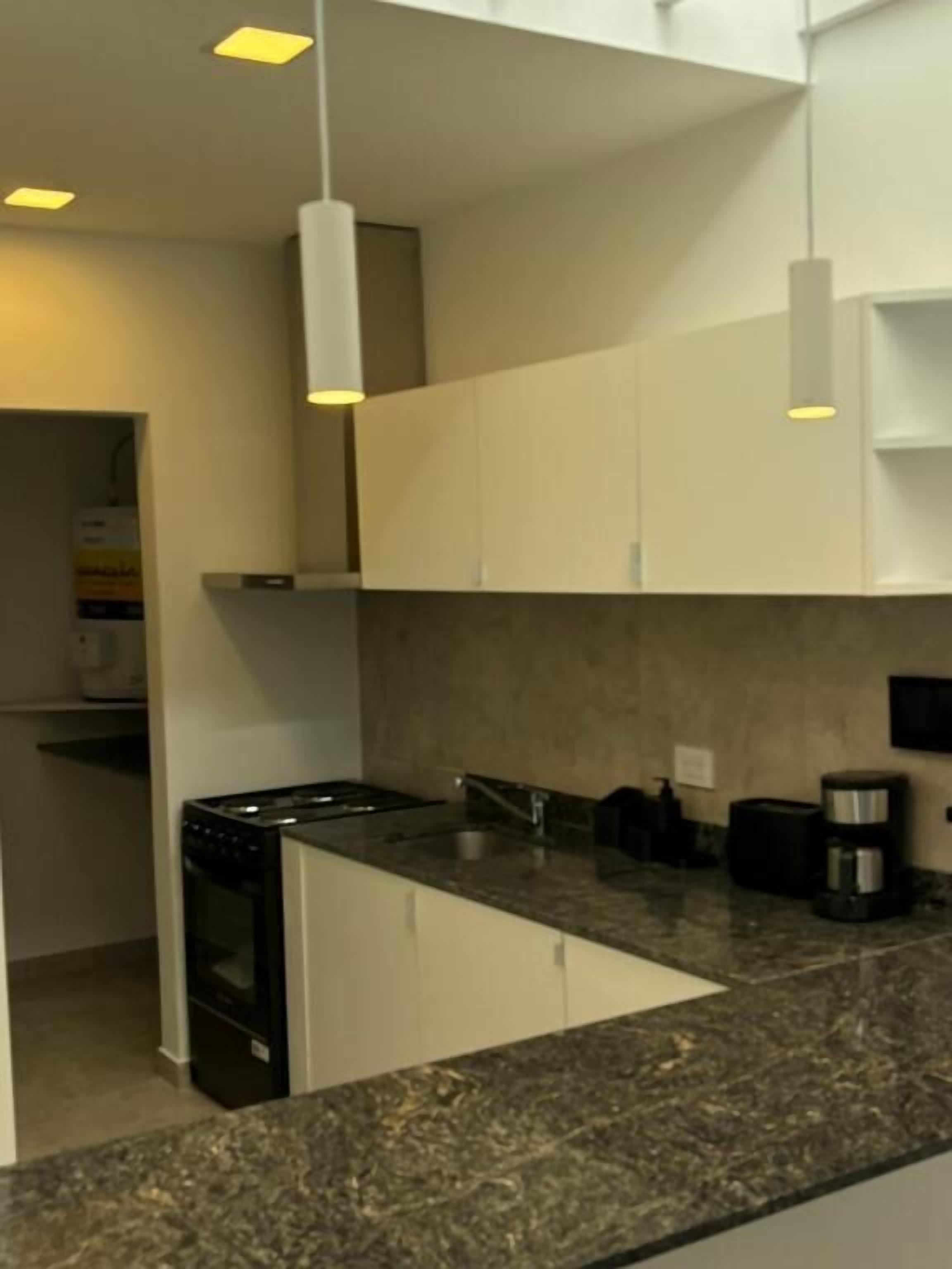 A modern kitchen with white cabinets, a granite countertop, and pendant lighting.