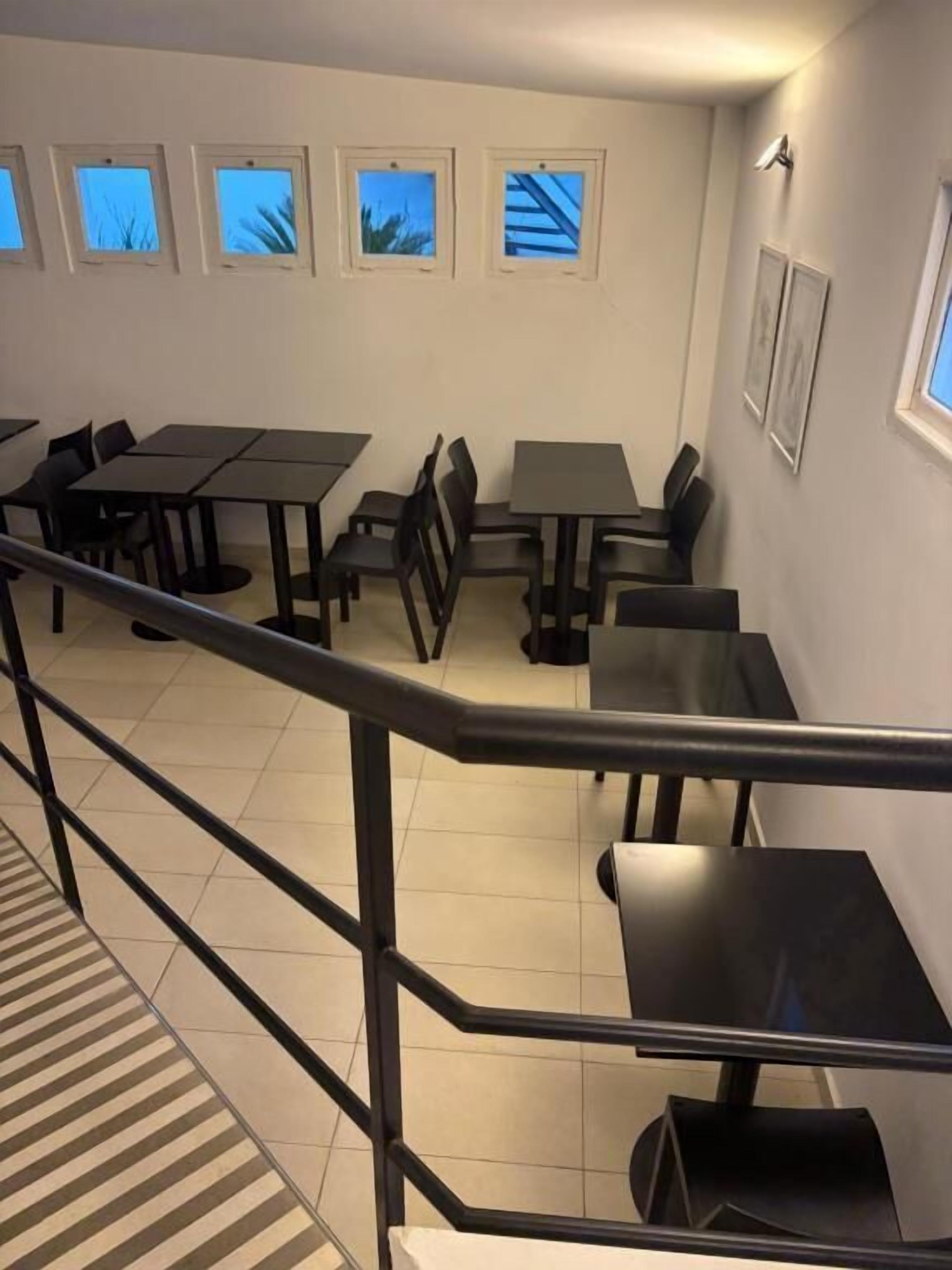 A dining area with tables and chairs, a staircase, and windows with views.