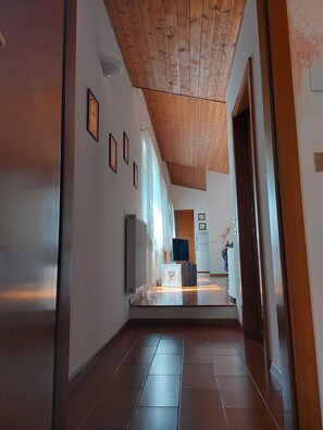 A hallway with a wooden ceiling, tiled floor, and framed pictures on the walls. - La Barchessa: A Plunge into Nature (Riva del Garda)